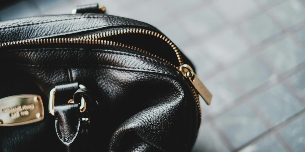 Close-up of a black patent leather purse with a gold zipper and hardware on a paved surface.