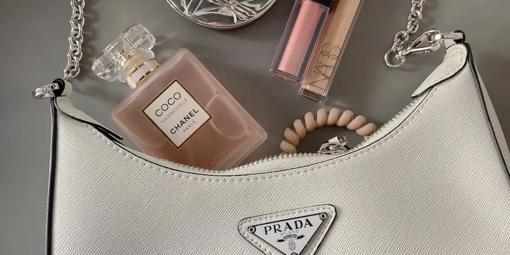 White leather handbag with a silver chain handle, surrounded by cosmetics and a perfume bottle.