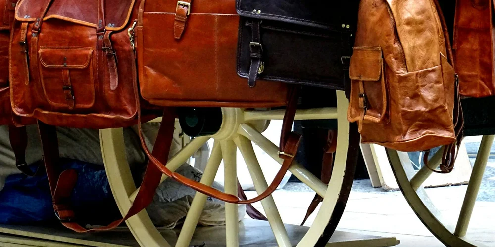 Leather bags and backpacks hanging from a display cart, showcasing handcrafted leather craftsmanship.