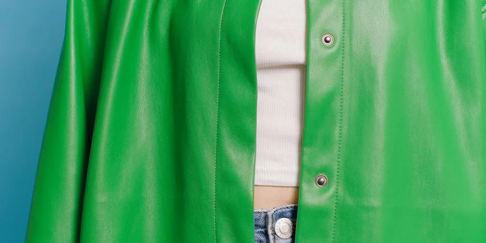 Close-up of a person wearing a bright green jacket over a white top and blue jeans, cropped at chest and waist.