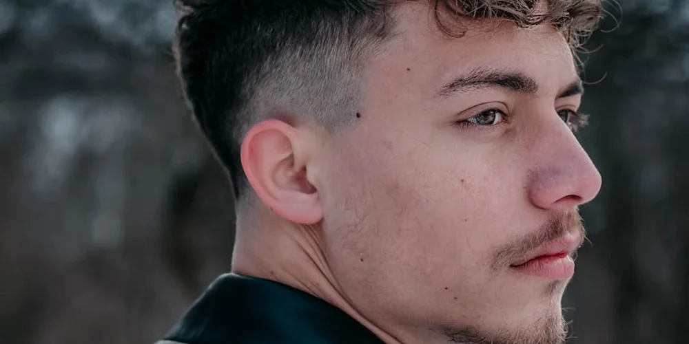 A young man in profile outdoors with a blurred natural background.