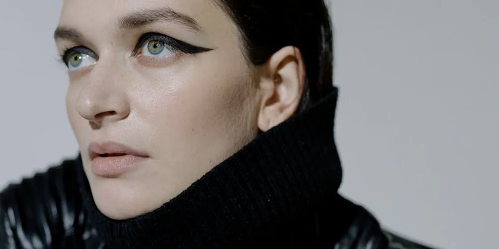Close-up portrait of a woman with bold winged eyeliner wearing a black turtleneck.