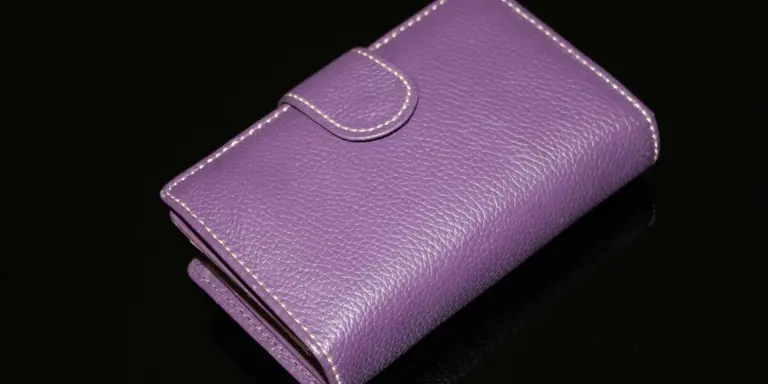 Purple leather purse with white stitching on a black background