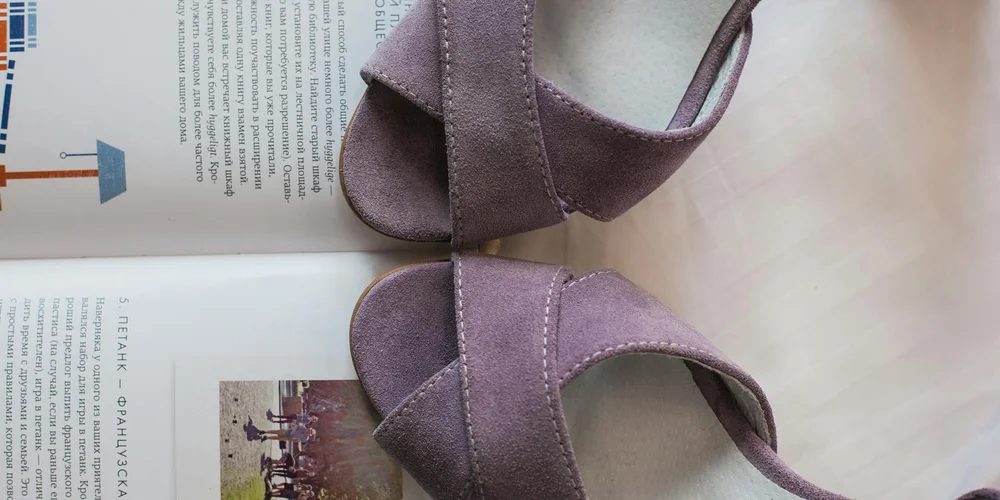 Two purple suede sandals placed on a magazine on a light surface, highlighting the suede texture.