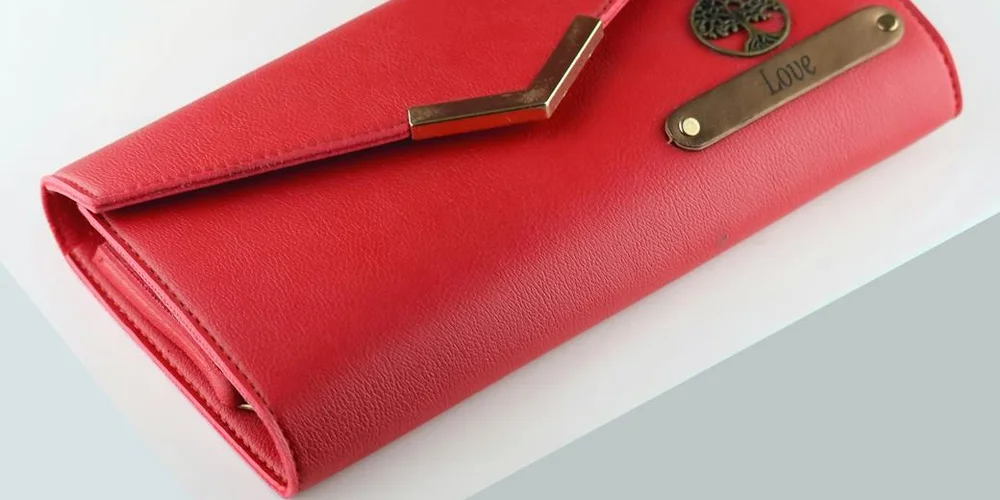 Close-up of a red leather wallet with metal hardware on a light background.