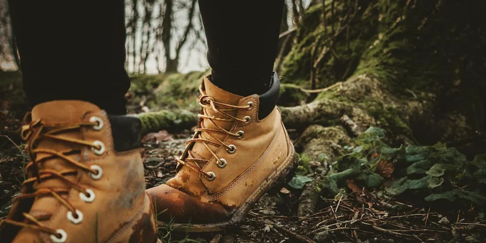 Close-up of tan leather Red Wing boots with laces, standing on a mossy forest floor.