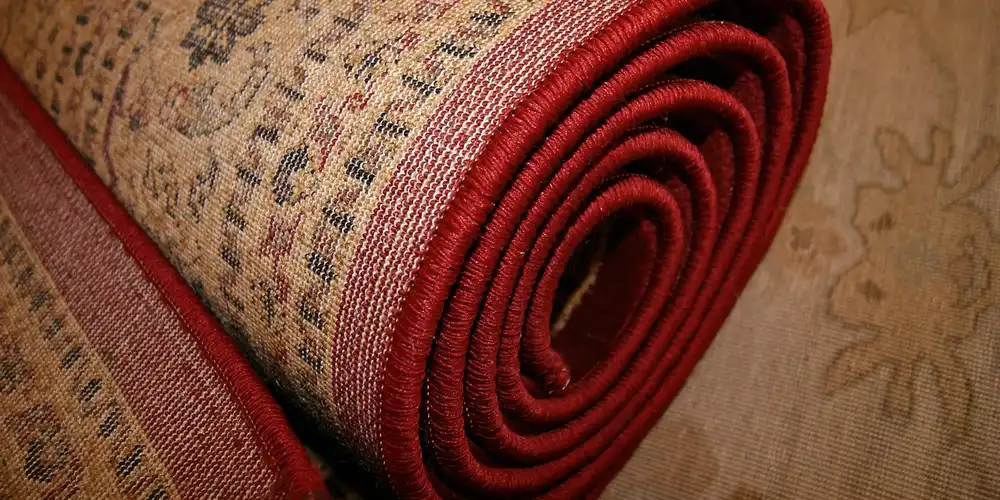Rolled cowhide or sheepskin rug with red edging laid on a patterned floor.