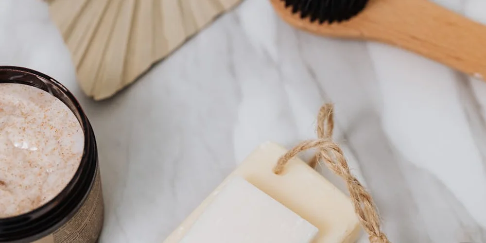 Jar of saddle soap paste with a wooden brush on a pale marble surface.