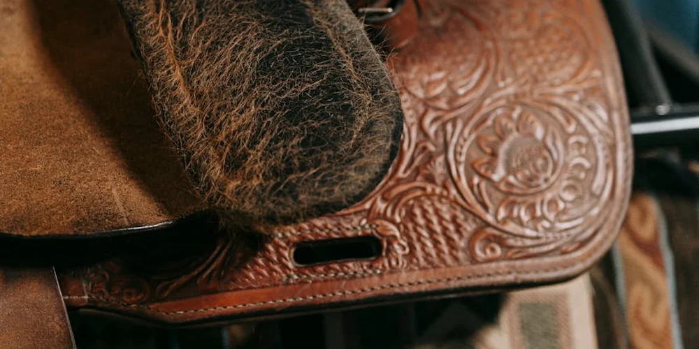 Close-up of a brown leather saddle with intricate tooling and visible wear.