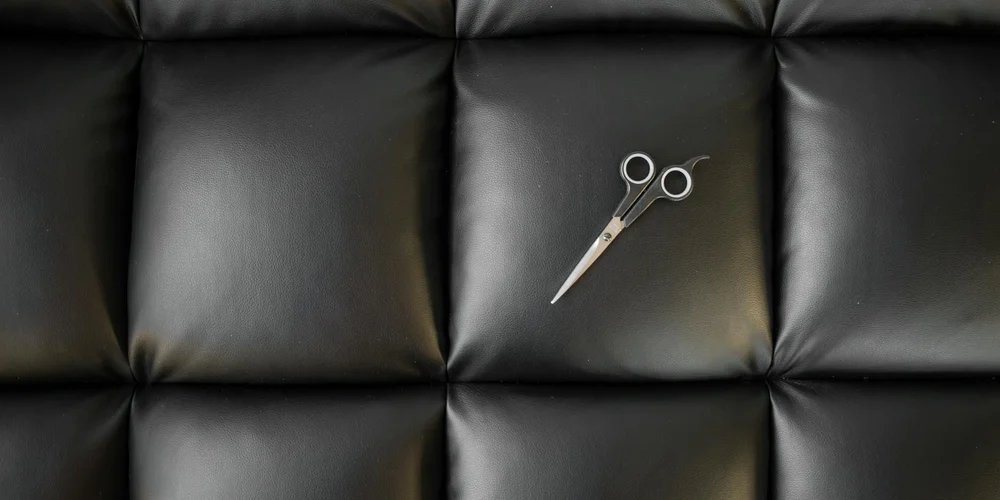 A pair of scissors resting on a dark, tufted leather surface.
