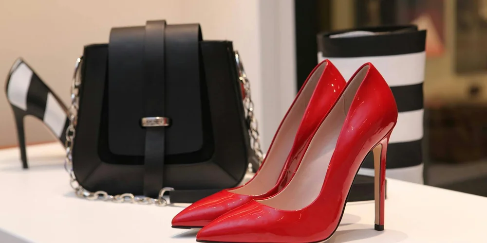 Red high-heeled shoes and a black handbag displayed on a clean surface, illustrating refined leather items with smooth finishes.