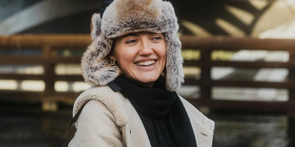 Smiling woman wearing a fluffy sheepskin hat and coat outdoors