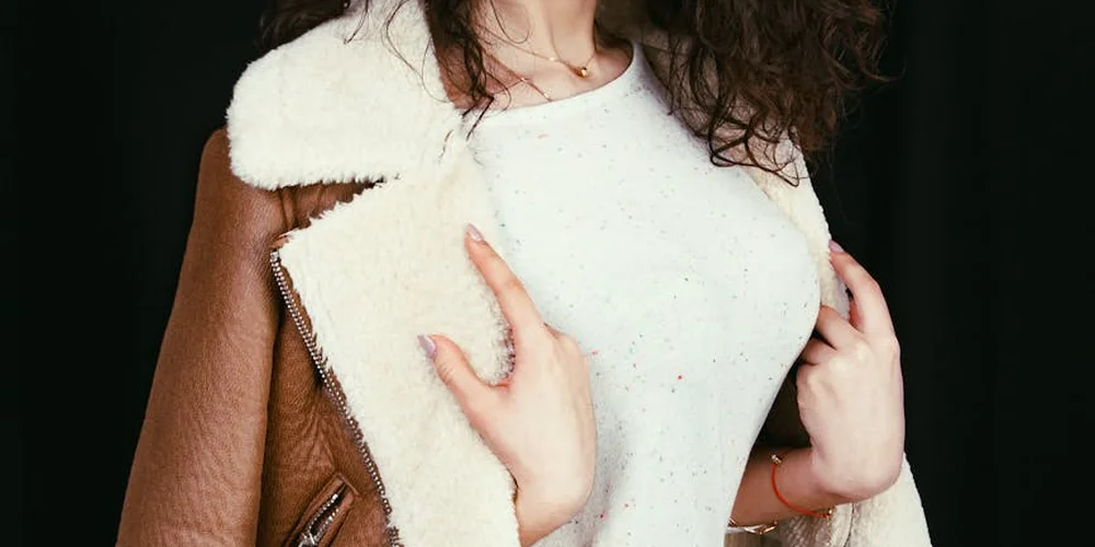 Close-up of a person wearing a cream sheepskin accessory draped over the shoulder, with a white top.