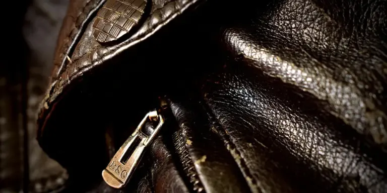 Close-up of dark brown shell cordovan leather with a metal zipper, showcasing fine grain and premium texture