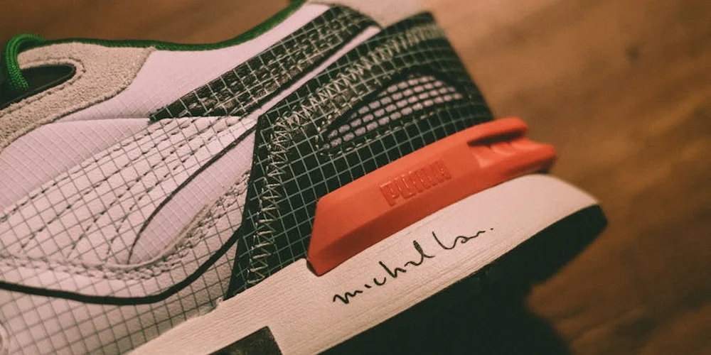 Close-up of a sneaker’s sole and heel area, highlighting tread patterns and a small handwriting-style mark on the midsole.
