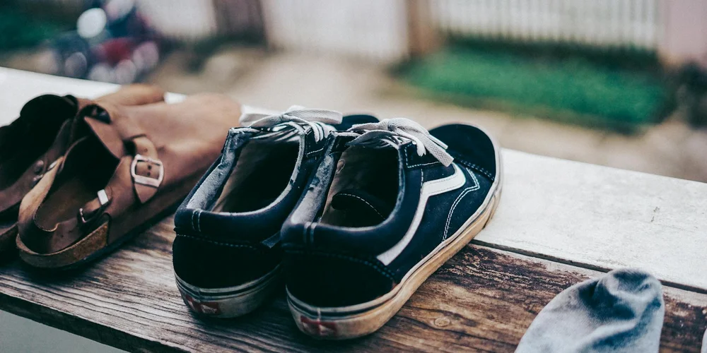 Two pairs of casual footwear—a sneaker and a sandal—rest on a weathered wooden surface outdoors.