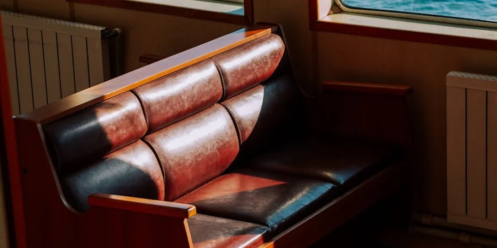 Leather sofa in a sunlit living room with brown and black panels, showing subtle wear on the seat cushions that could indicate a small tear.