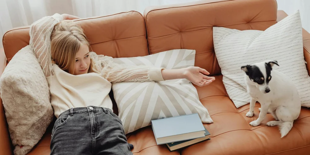 A woman relaxing on a brown leather sofa with a small black-and-white dog nearby