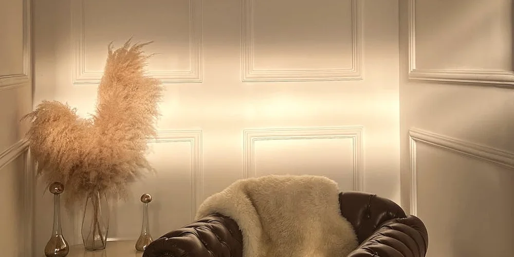 Dark brown leather sofa with a light cream throw in a paneled beige room with pampas grass in a vase nearby.