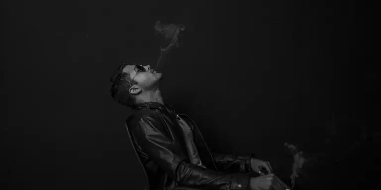 Person wearing a black leather jacket in a dark room, exhaling smoke.