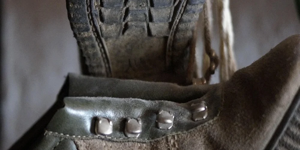 Close-up of a suede boot or jacket strap with metal rivets and a rugged tread, illustrating stiff suede texture.
