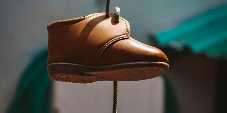 Brown suede boot suspended in midair with a blurred background, illustrating mud-stain removal for suede.