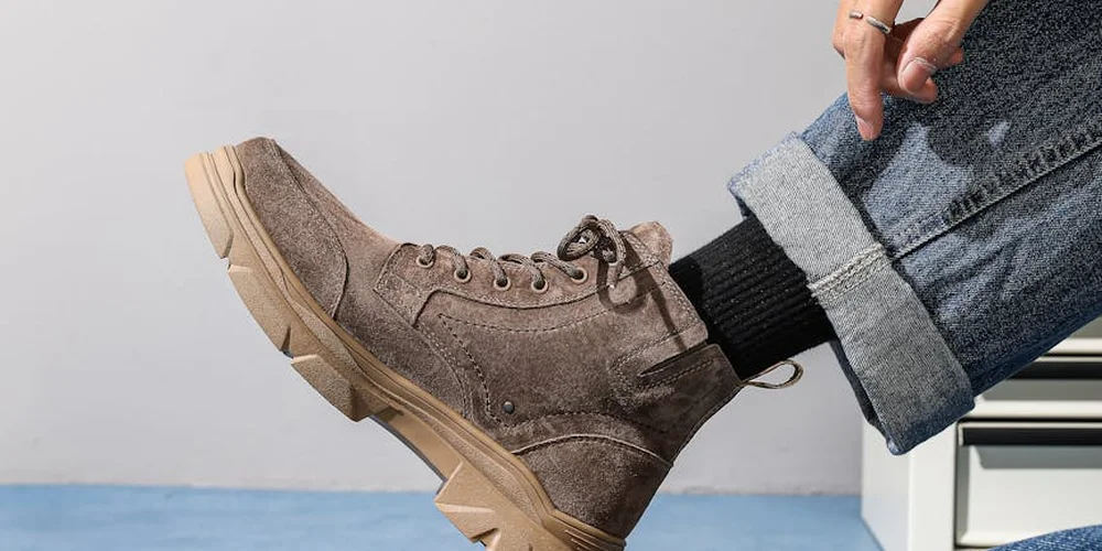 Brown suede boot with laces and rolled-up jeans against a light background.