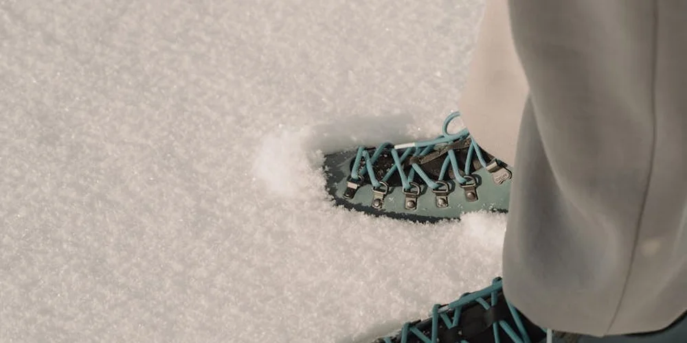 Close-up of teal suede boot laces in the snow, showing snow and salt exposure on the material.