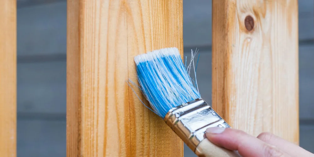 A blue-bristle brush is being used on a wooden surface, representing selecting the right cleaning tool for suede care