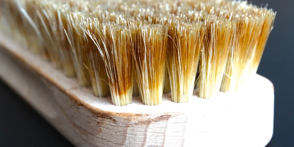 Close-up of a wooden-handled suede brush with dense, light-tan bristles