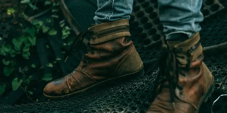 Brown suede boots worn by a person standing on a textured surface outdoors.