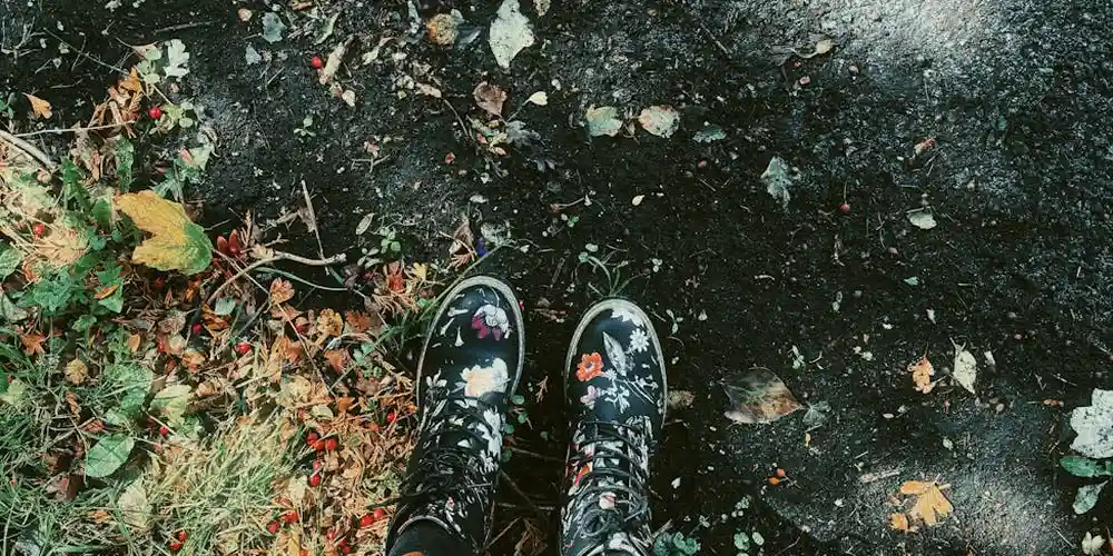 Top-down view of black suede boots on a damp pavement with fallen autumn leaves.
