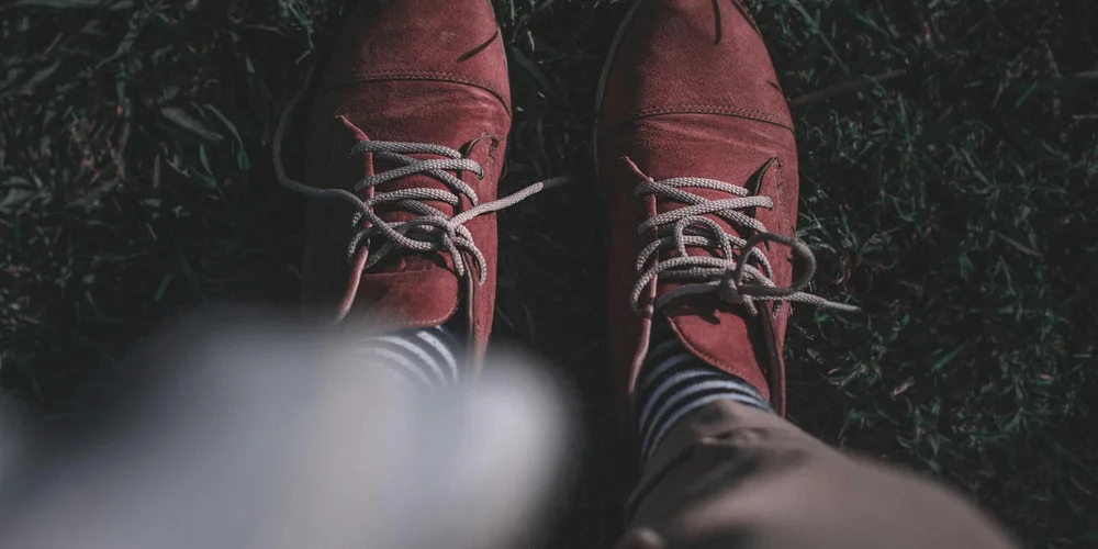 Overhead view of burgundy suede shoes resting on grass