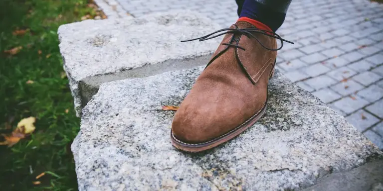 Brown suede ankle boot resting on a rough stone step outdoors