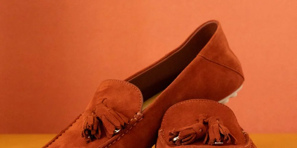 Two brown suede loafers on an orange background.