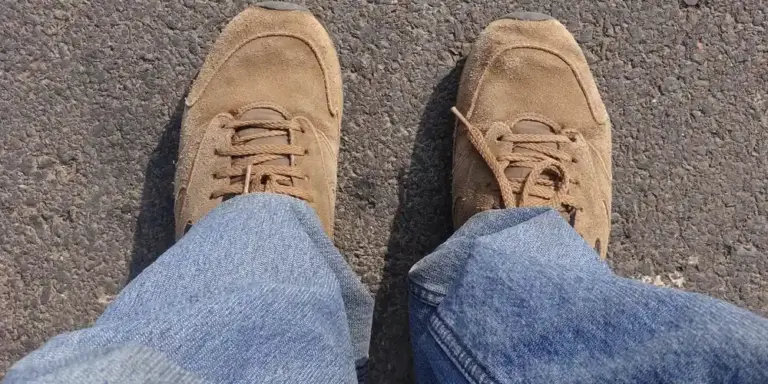 Top-down view of a pair of tan suede shoes wearing jeans, standing on a paved surface