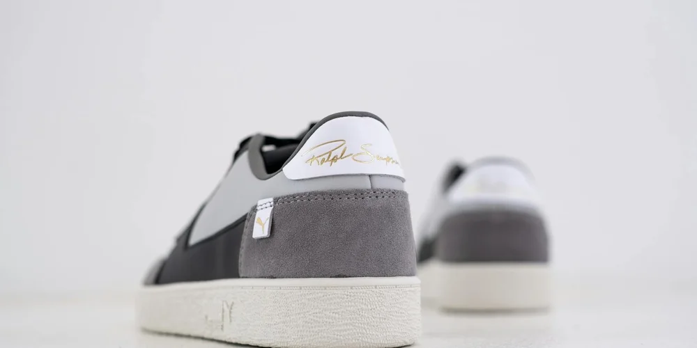 Close-up of gray suede sneakers with white soles, photographed from the back on a light background.