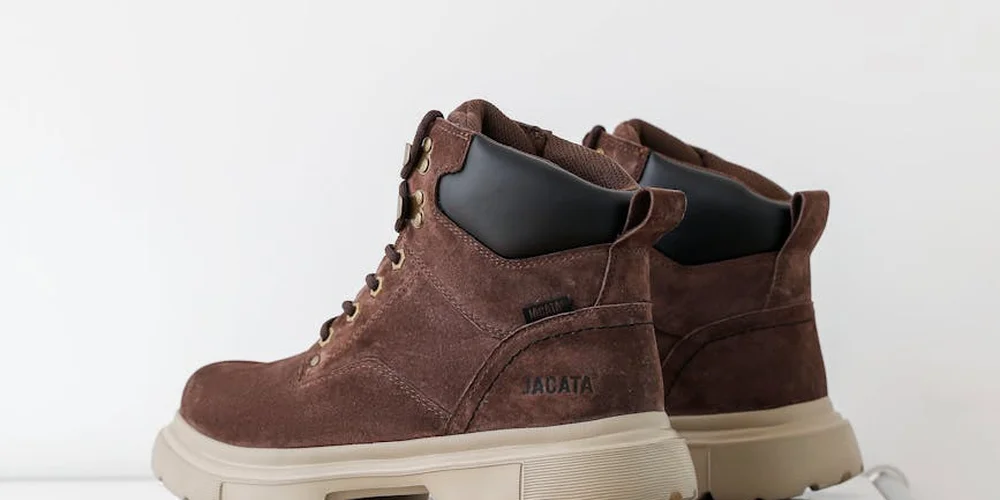 Brown suede military-style boots with cream rubber soles and laces, photographed on a pale background.