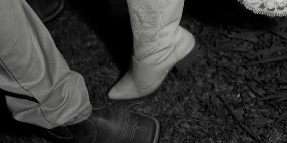 Black-and-white close-up of white suede boots standing on a dirt surface