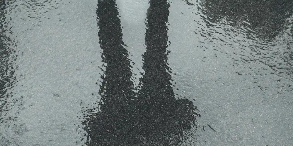Reflection of two legs in a puddle on a wet street, hinting at rainy spring weather and fashion choices.