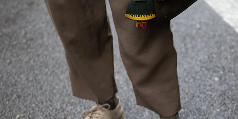 Close-up of brown suede fabric on a pair of pants with a textured pavement surface in the background.