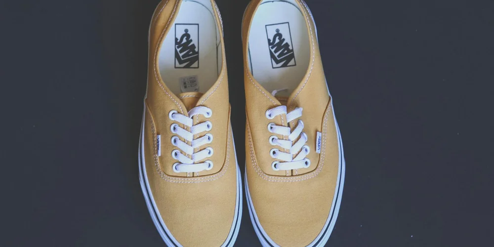 Top-down view of tan suede Vans sneakers with white laces on a dark background.