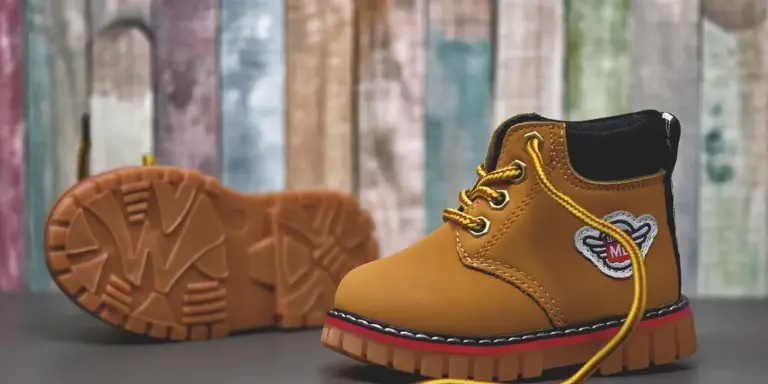 Tan suede boots with yellow laces and rugged soles on a wooden backdrop