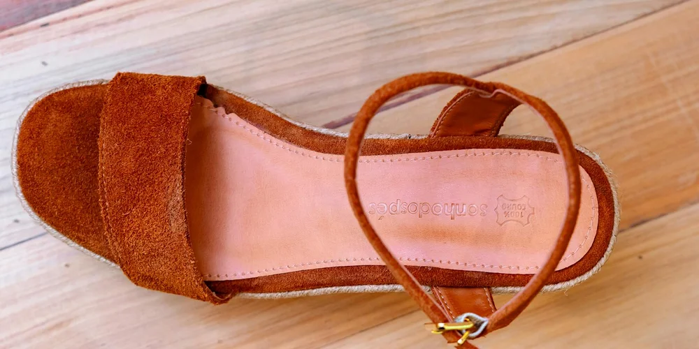 Brown suede sandal resting on a light wooden surface