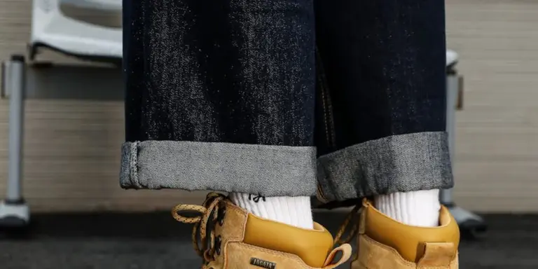 Close-up of tan suede shoes with white socks and rolled denim cuffs, highlighting suede texture and fabric details.