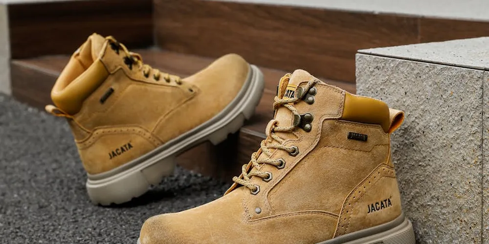 Two tan suede boots resting on a textured pavement with a concrete curb nearby.