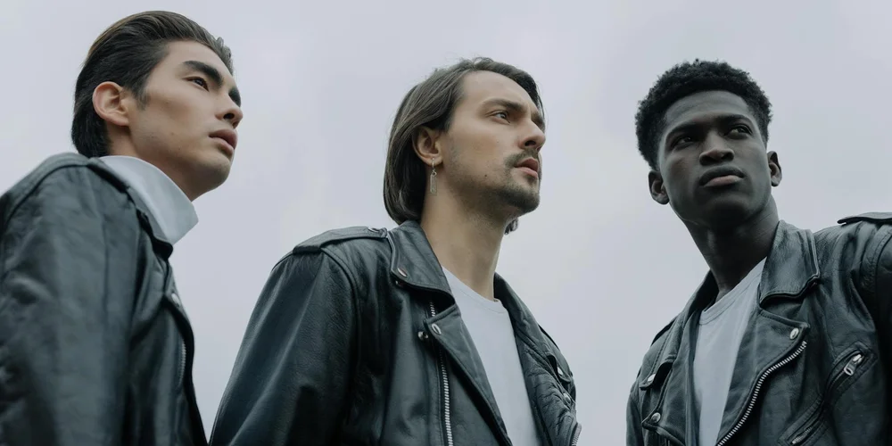 Three people wearing black leather jackets looking upward against a cloudy sky.