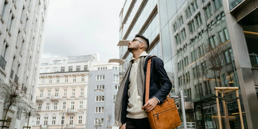 Man walking in an urban city street with a brown leather bag.