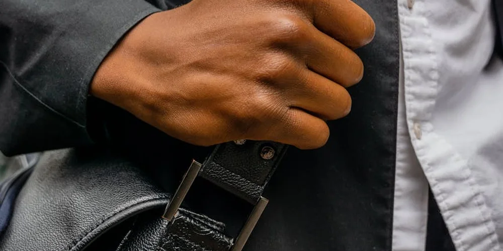 Close-up of a hand gripping a vintage leather bag handle, suggesting wear and the need for repair.