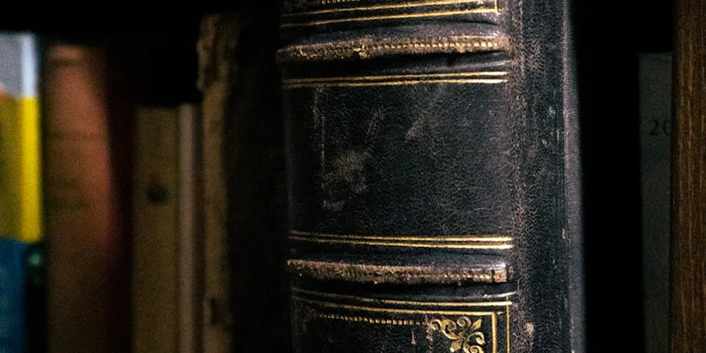 Close-up of a worn black leather book binding with gold tooling, showing age-related wear.